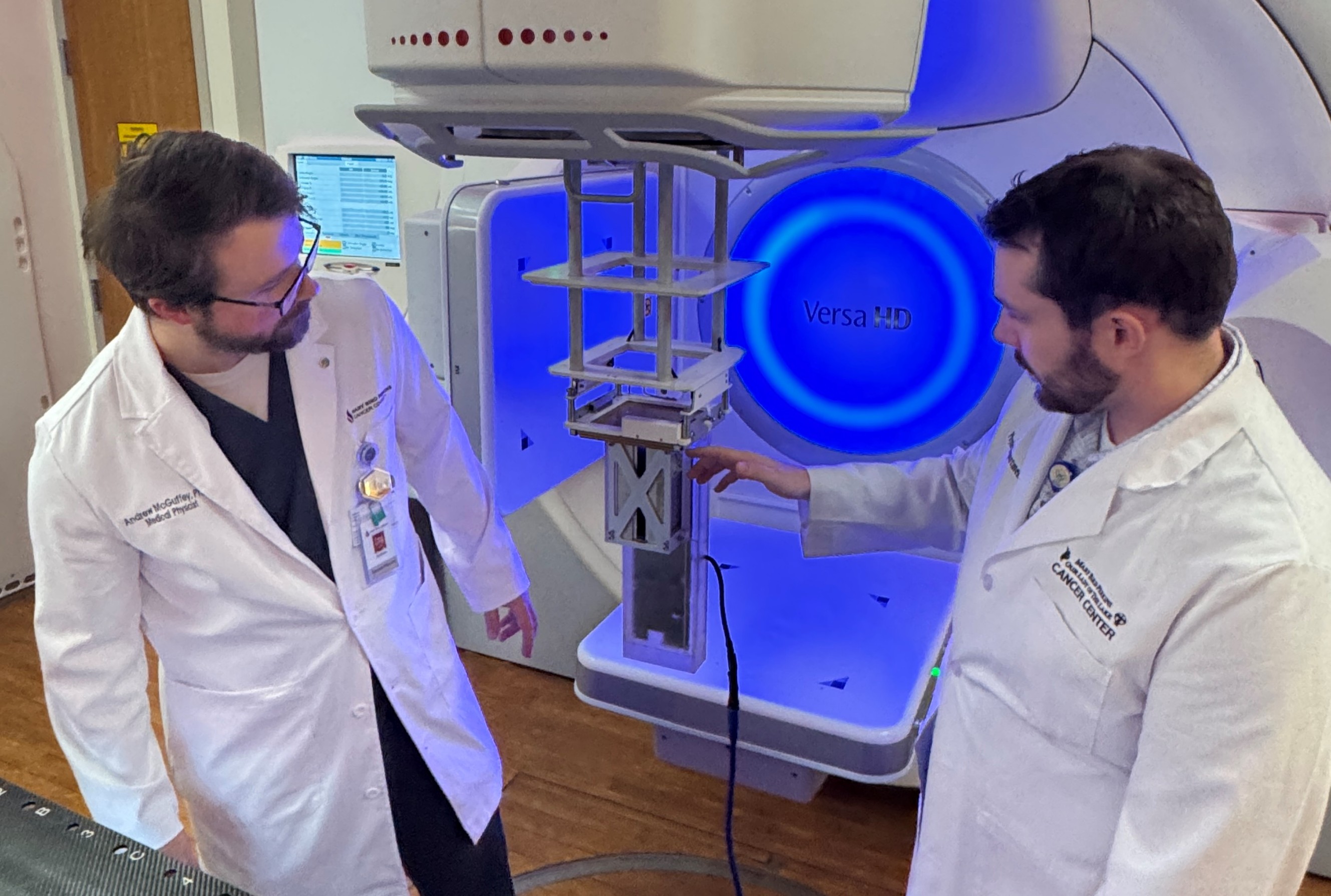 Graduate student Mason Heath (R) shows Dr. Andrew McGuffey (L) attachment of real-time energy spectrometer* to bottom of Elekta electron applicator for use in electron beam tuning.